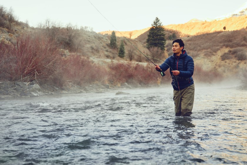 An Asian Korean man, fly fishing on the Provo River in Utah during winter.