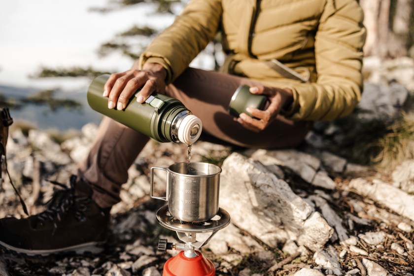 Cropped shot of an unrecognisable black woman sitting on the top a hill and having tea break during her hike in the mountains.