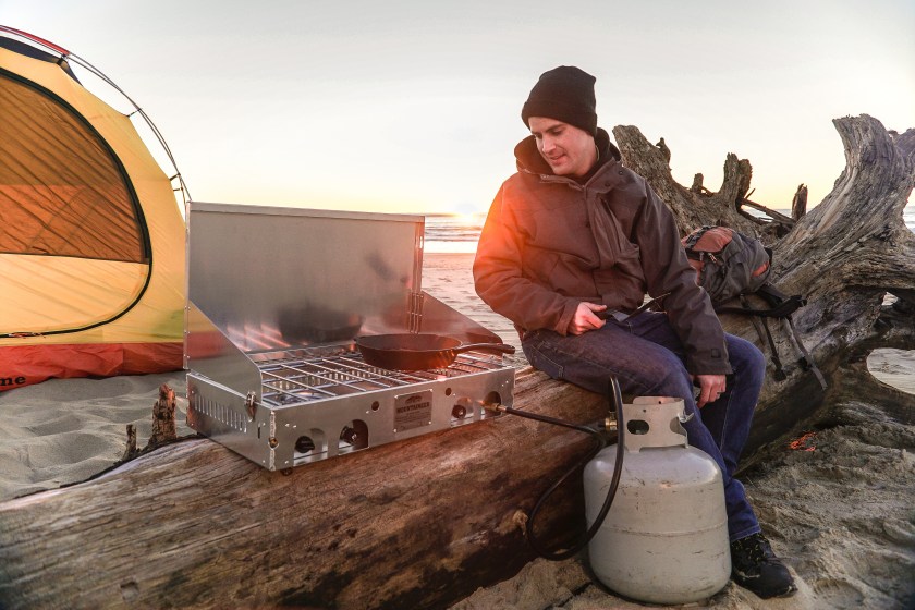 Person sitting on a ledge next to a CampChef Stove