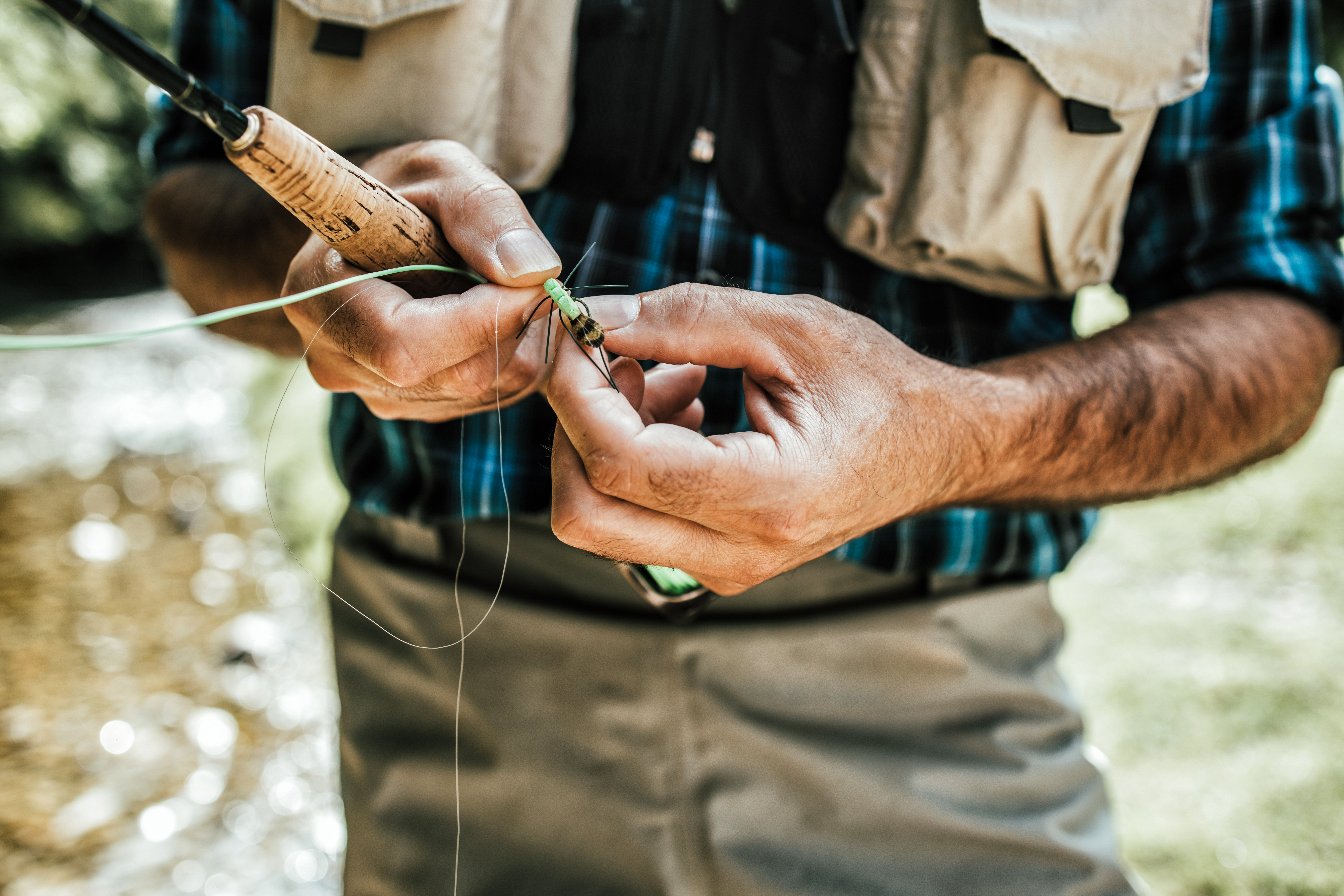 Close up shot of senior fisherman's hands tying a fly for fishing. Fly fishing concept. View from above. High angle view over shoulder.