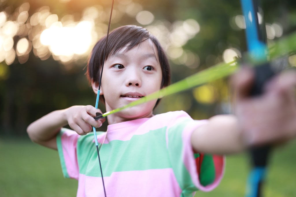 Little boy shooting bow in forest