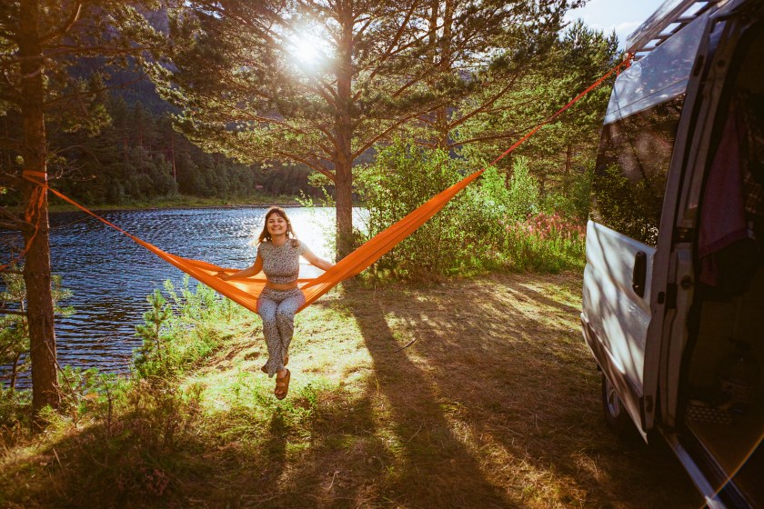 Young Caucasian woman resting in hammock near camper van in forest.