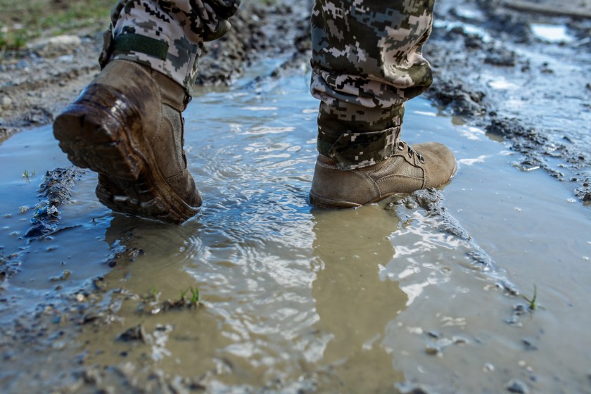 Brown military boots on mud and puddle. Armed Forces of Ukraine. Ukrainian soldier.