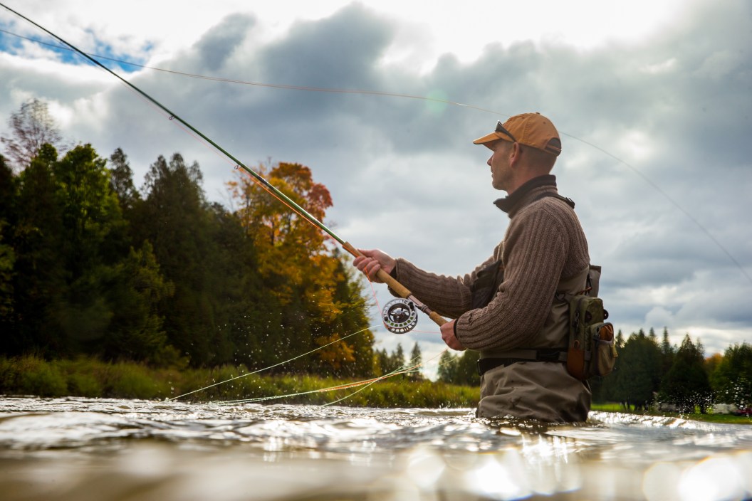 A man casts his fly rod into a river during the autumnA man casts his fly rod into a river during the autumn