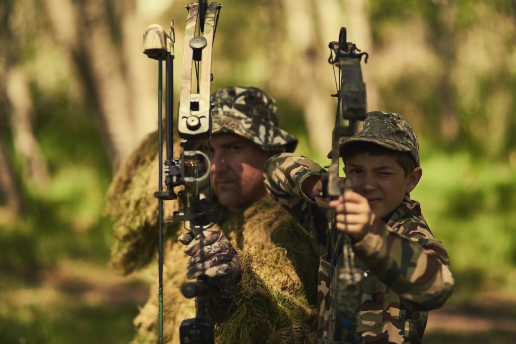 Portrait of a father and son in camouflage hunting with bows and arrows in the woods