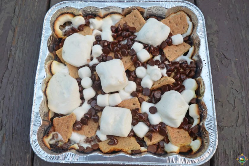 A foil baking tray with graham crackers, chocolate, and marshmallows