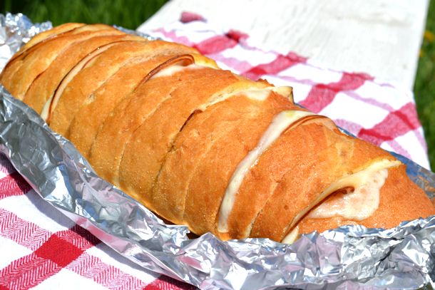 A ham and cheese pull apart bread in a foil bowl on a checkerboard tablecloth