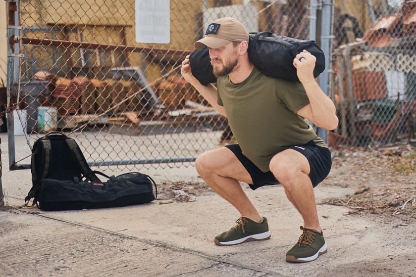Person in a weighted squat next to a GORUCK pack
