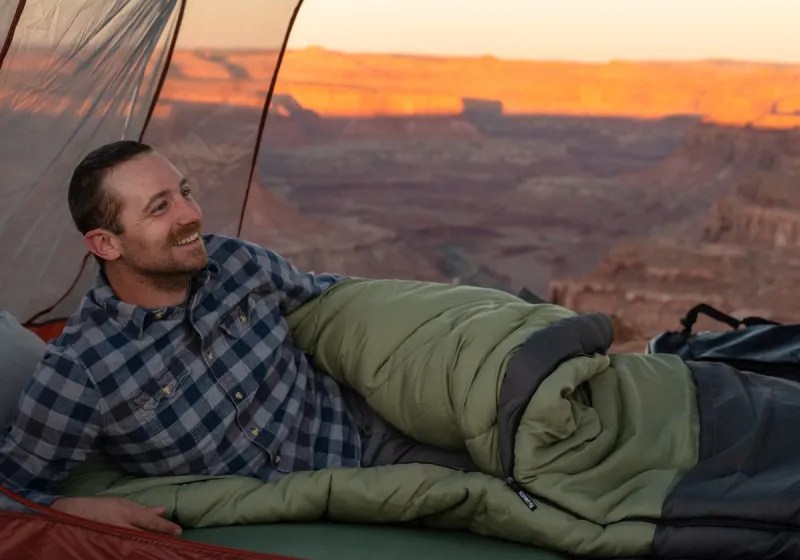 A person inside a camping tent sleeping with a green sleeping bag