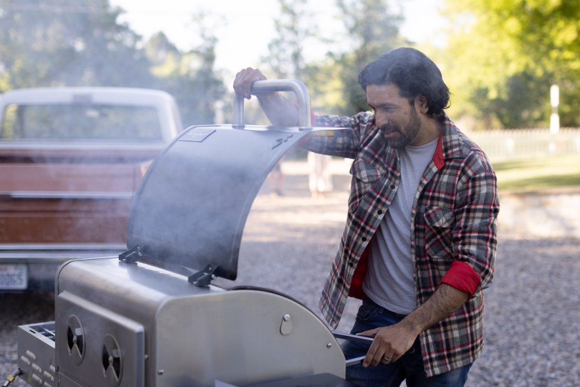 Person wearing a flannel opening a silver Camp Chef grill