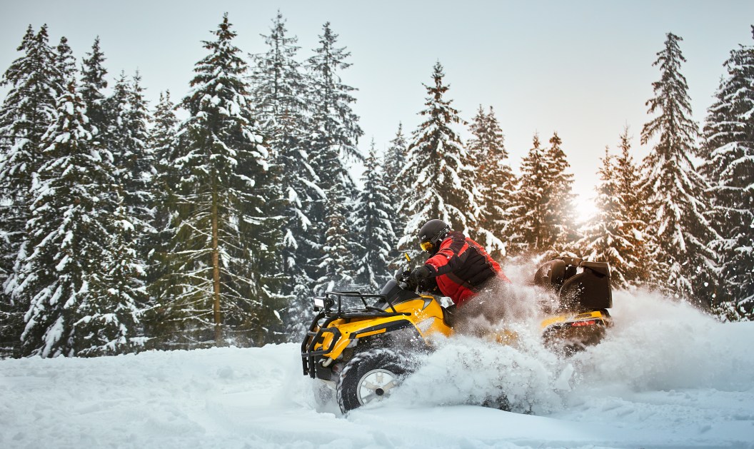 A man is riding an ATV in winter on the snow in his helmet.