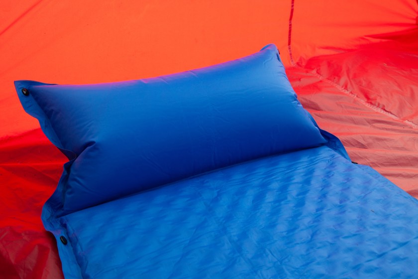 A blue self inflating blow-up mattress pad is placed in a red tent to provide a comfortable sleep to campers or those with a bad back