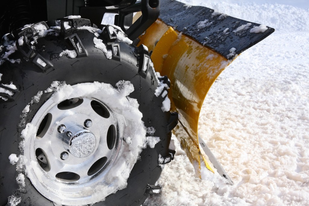 Plowing snow with a blade mounted on the rear of four-wheeler (ATV). Close up.