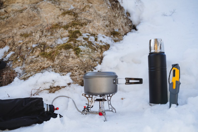 Tourist utensils, cooking in nature in the winter season, a burner with a pan stands on the snow, a thermos with tea, a bushcraft knife. High quality photo