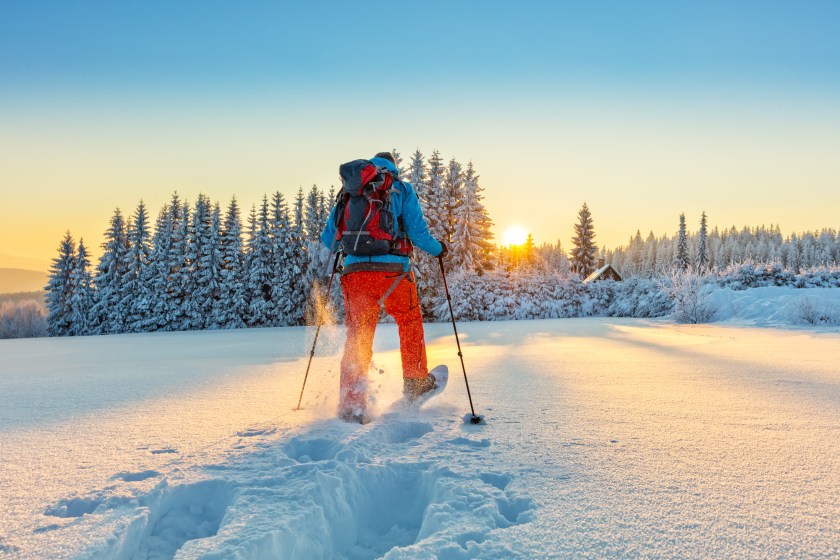 Snowshoe walker running in powder snow with beautiful sunrise light. Outdoor winter activity and healthy lifestyle