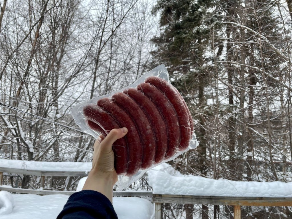 Person holding moose sausages in front of a snowy background