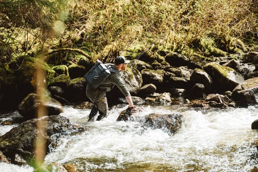 Person hiking inside a waterfall wearing a YETI cooler backpack