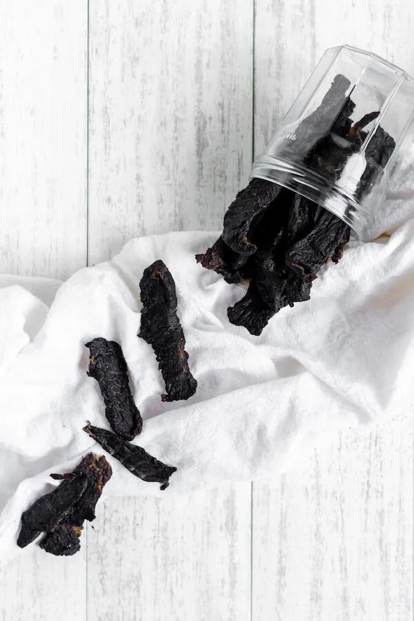 Dried homemade deer jerky spread out over a white wooden background