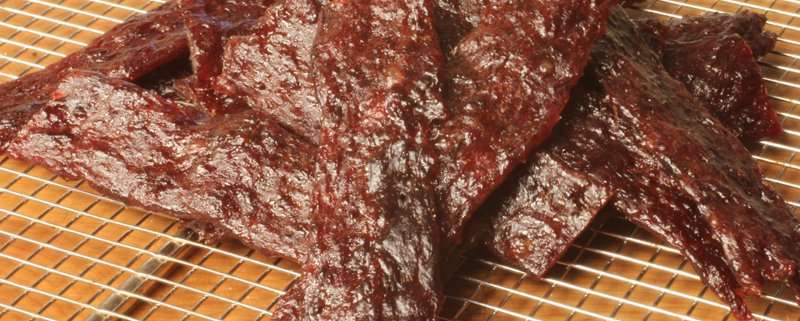 A pile of marinated venison jerky strips on a grill tray