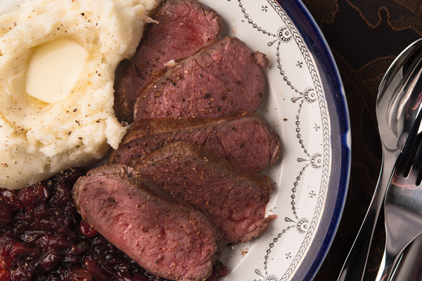Venison with cranberry sauce next to mashed potatoes