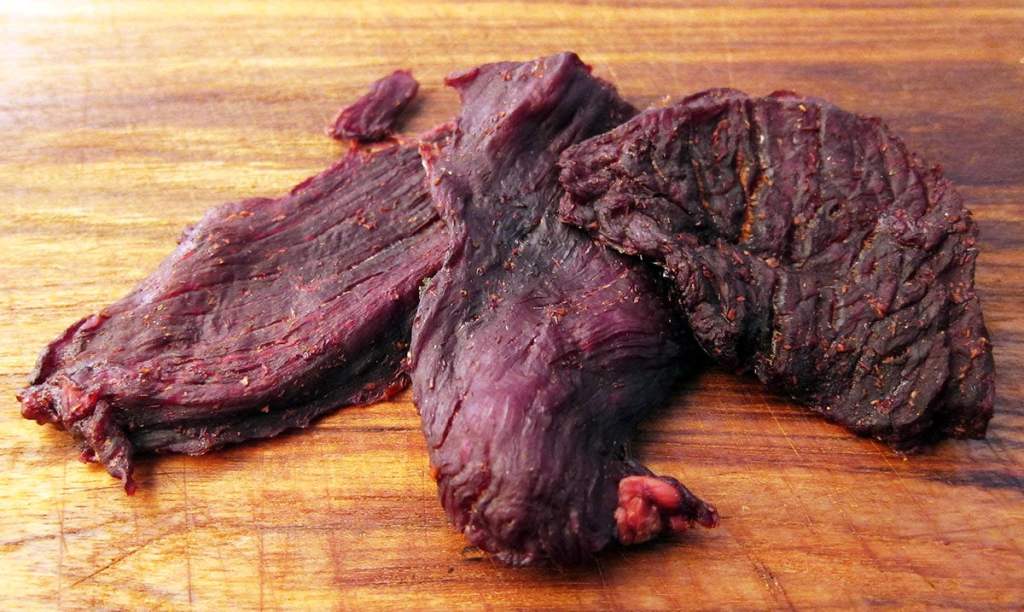 Three pieces of venison jerky on a wooden background