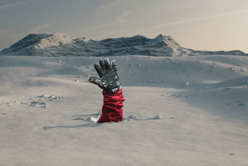 Hiker stretching out his snow covered hand to signal help because of snow avalanche . Danger extreme concept