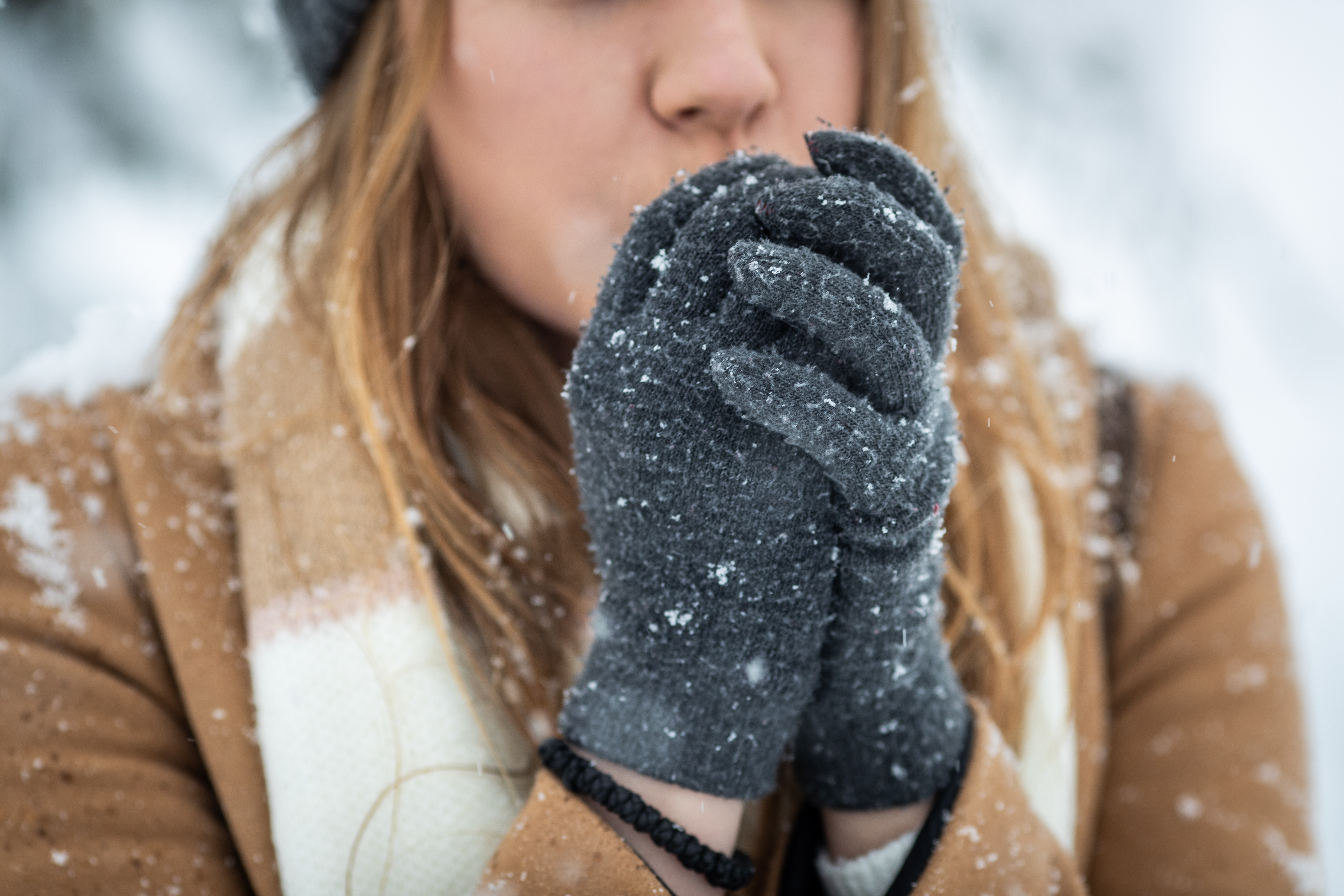 Young woman blowing arms to warm them because of the cold weather