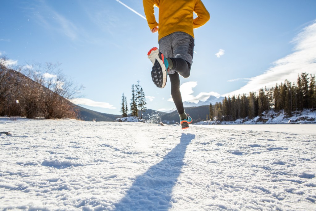 Sportive young man exercising trail running on mountain trail in Alberta, Canada. People body conscious and heathy lifestyle concept. Winter