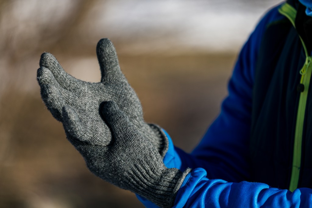 Man putting winter gloves on, he is wearing red jacket and black hat.