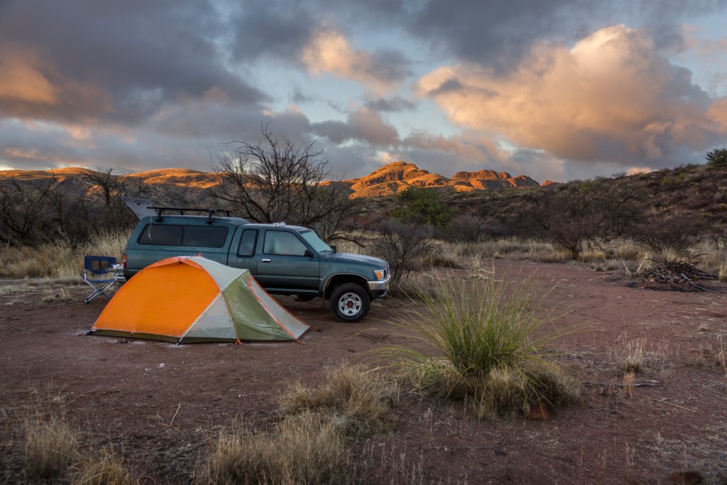 At sunrise after a freezing night, frost rolls off the sides of an orange tent next to a pickup truck camping on BLM Lands in the Galiuro Mountians and Coronado National Forest near Muleshoe Ranch Cooperative Management Area in Southern Arizona.