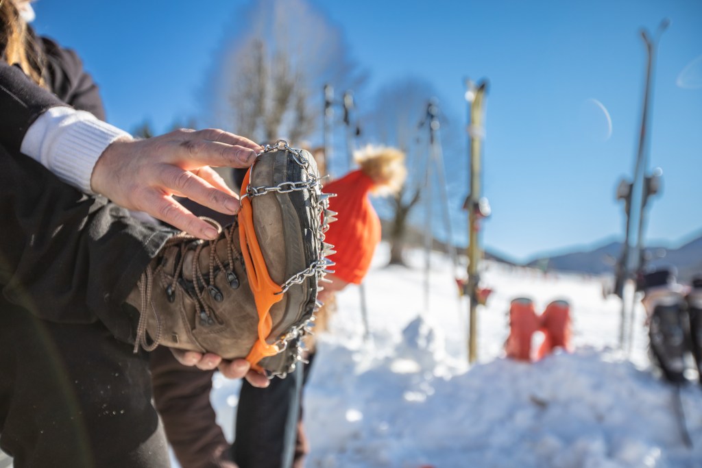 Close-up of Man Sitting By a Ski Slope With Crampons on Hiking Boots.