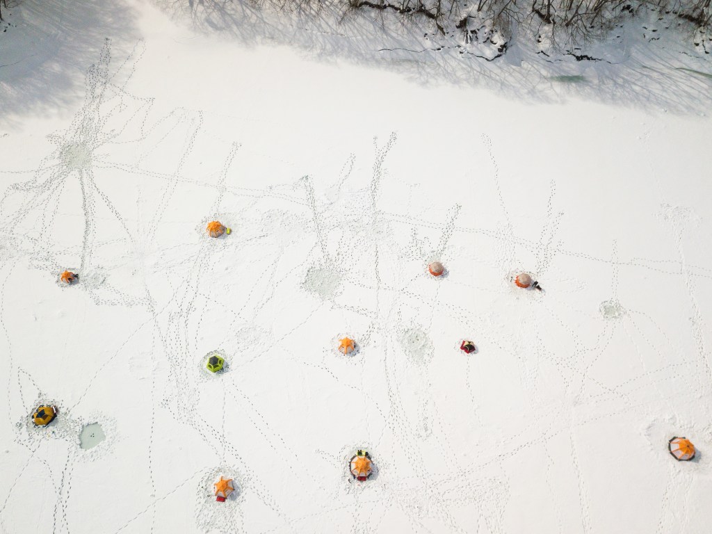 A high angle wide view over frozen lake in North Japan of many tents pitched on the lake for people to enjoy ice fishing.