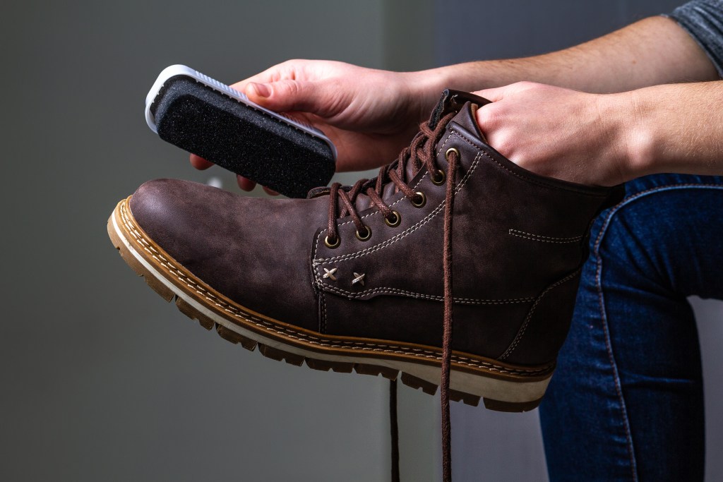 Person is cleaning men's suede casual boots with brush. Shoe shine. Footwear moisture and dirt protection