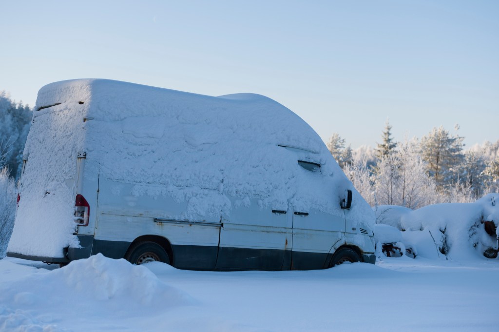 White minibus covered with thick layer of snow in the field