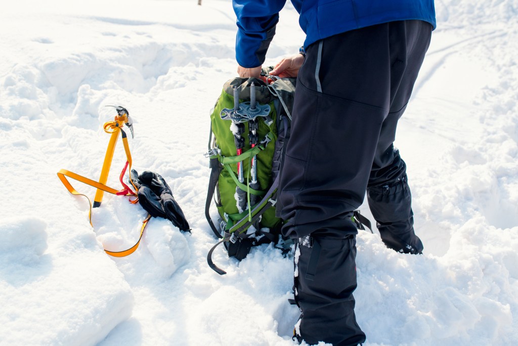Ice climber packing a bag outside in the snow, preparing for a winter hike. Tottori, Japan. February 2016