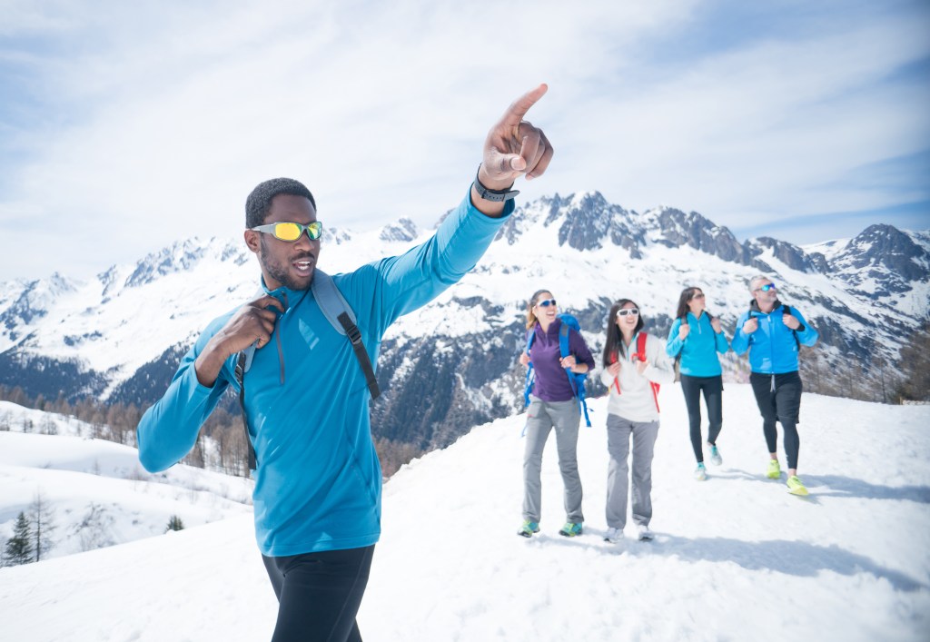 Happy group of friends hiking in the snow mountain and man pointing away