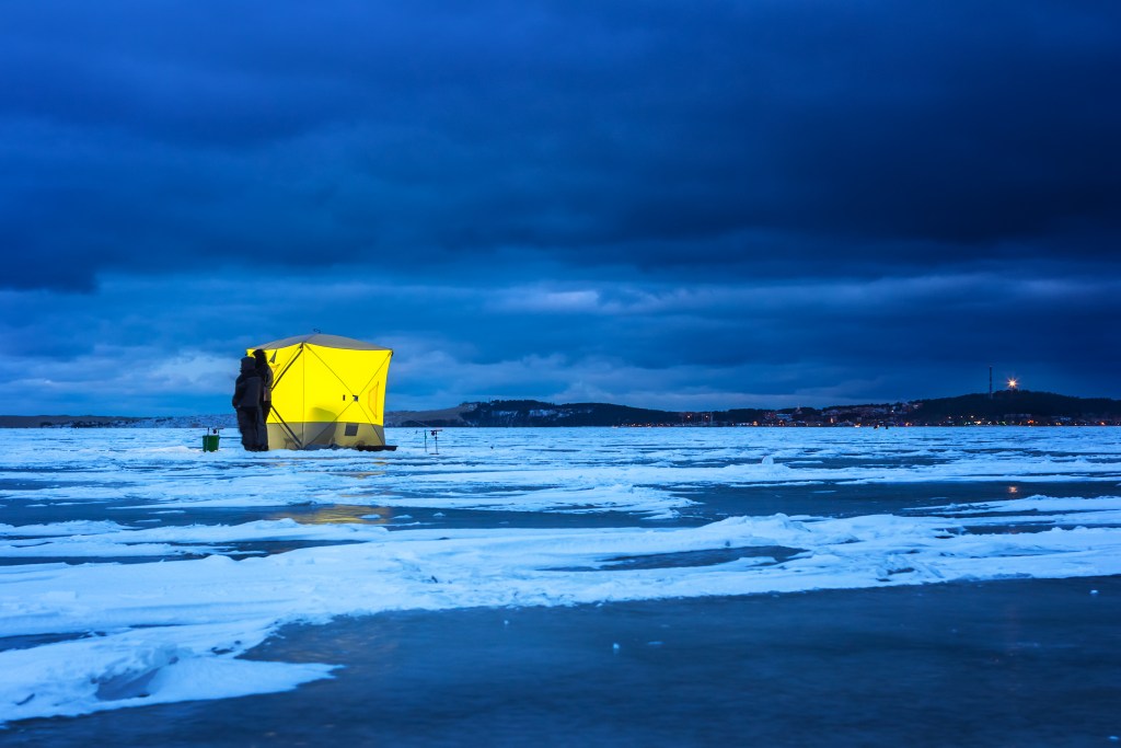 Night ice fishing. Yellow fishing shelter on the ice at night, Nida, Lithuania