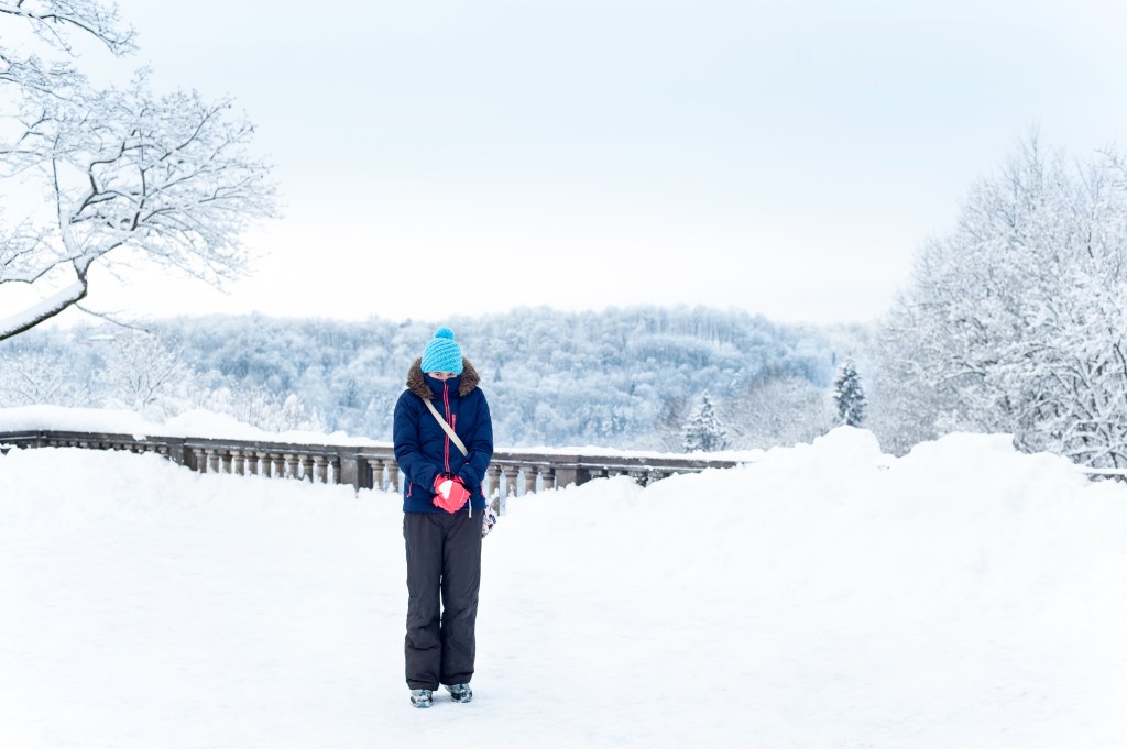 Warmly clothed freezing girl on background with spectacular winter view with snowy frozen woodland on hills in Sigulda. Latvia. Baltic states. Vibrant outdoors horizontal image.