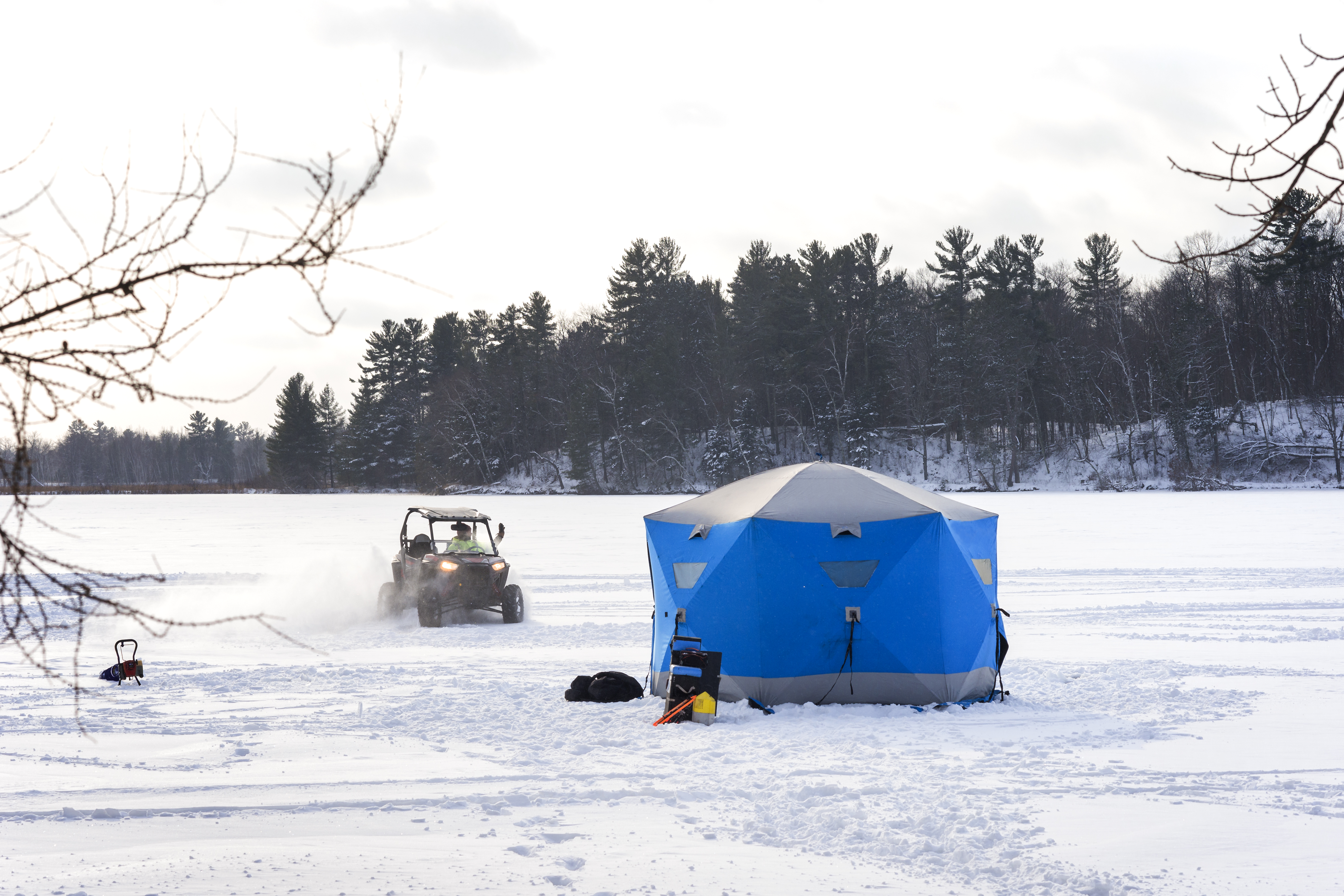 Four wheeler vehicle approaches a blue ice fishing hut erected on a frozen lake on a subzero winter day in northern Minnesota, USA