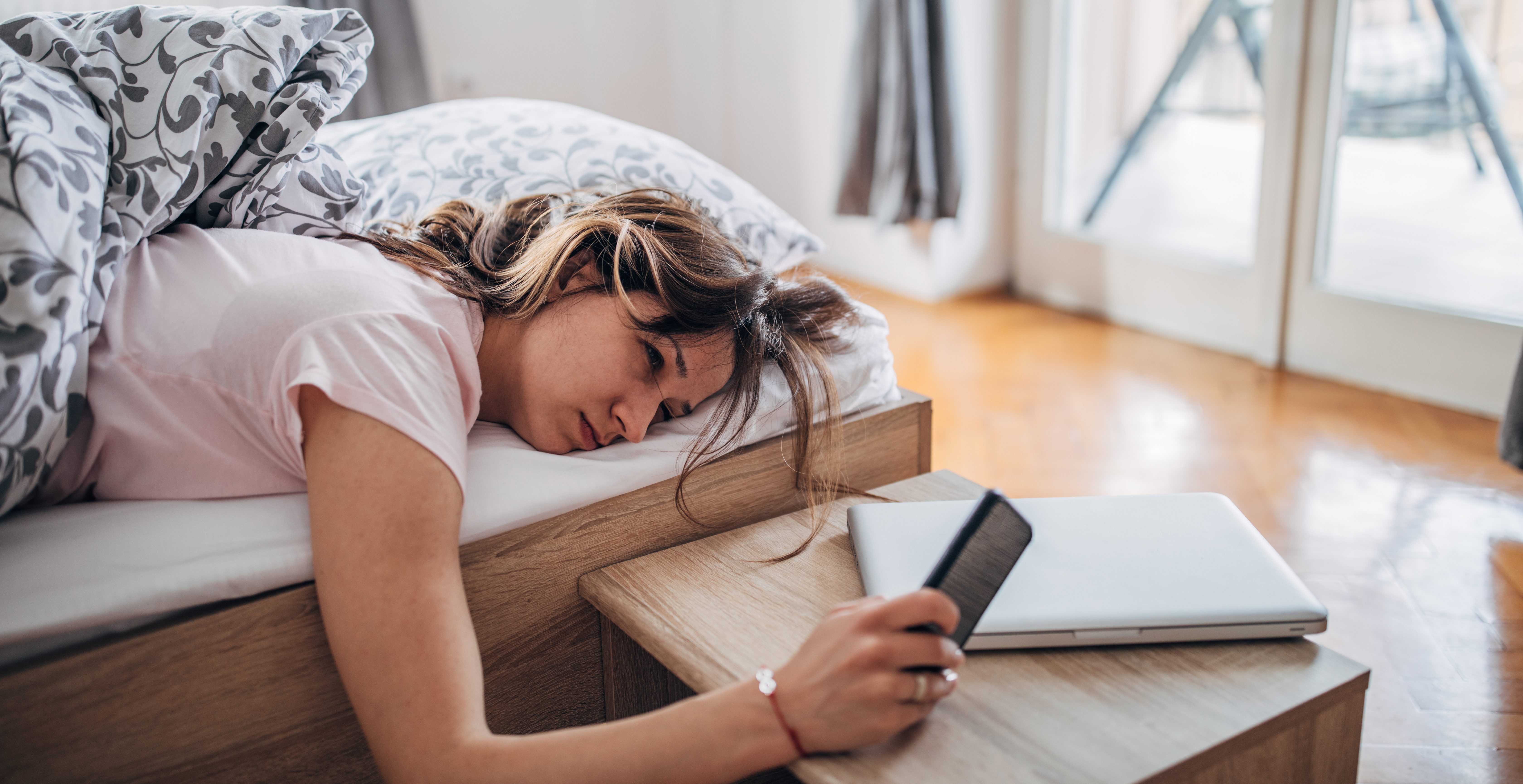 daylight savings time- Young woman is waking up and looking at her smart phone.